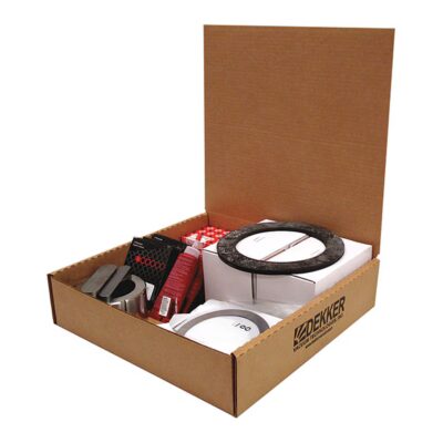 An open cardboard box labeled "Dekker Vacuum Technologies DV0080D-KB4 Major Spare Parts Kit (P/N 4700-1000-023)" contains various packaged items, including a round black object, a white item, metal parts, and red and black boxes.