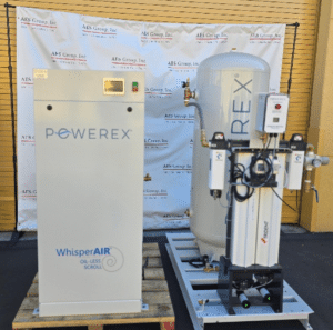 Two large industrial machines, including a Powerex Laboratory Compressed Air System Model SED1007-DD-AES-SPL (P/N SED1007-DD-AES-SPL) and a unit labeled “WhisperAIR,” are positioned outdoors on a blacktop, with an AES Group, Inc. branded backdrop and a yellow roll-up door in the background.