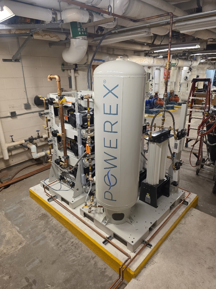 A Powerex industrial air compressor system mounted on a yellow-bordered concrete base in a utility room.