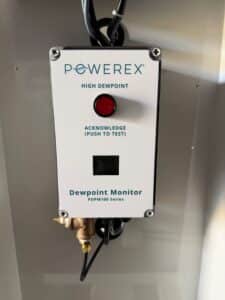 Powerex, Inc. Dew Point Monitor (P/N PDPM1004AJ) control panel featuring a red indicator light, an “Acknowledge (Push to Test)” button, a digital display, and a brass pipe fitting at the bottom.